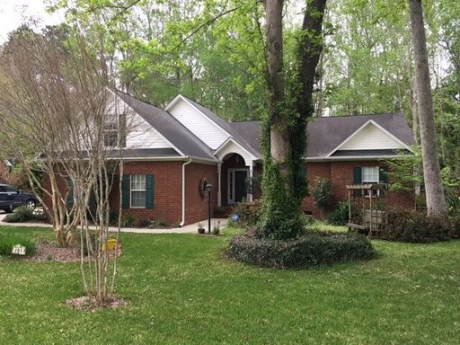 An image of the one story brown house behind the tree and large garden in front of it 