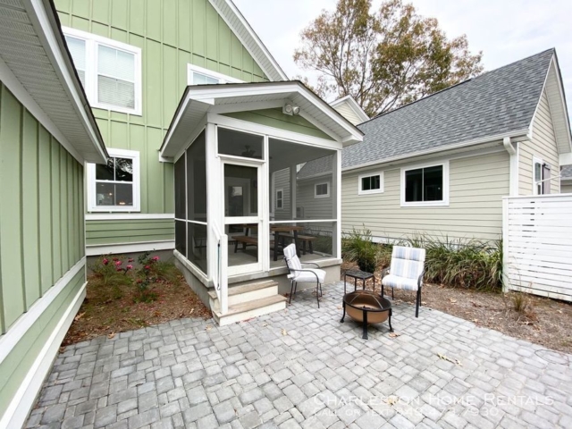 Backyard of a two story green colour house with chairs and outdoor cooking stove