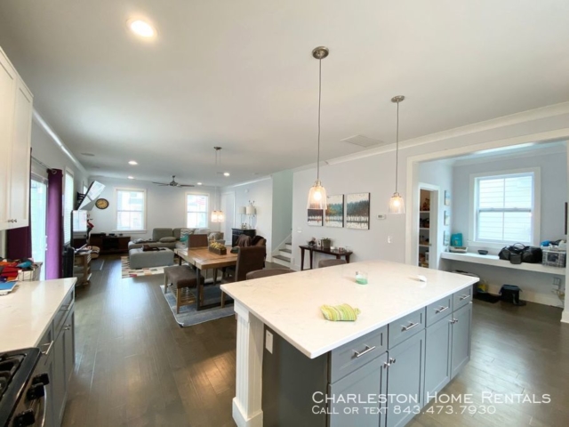 An inside image of a well furnished living room with hanging tv above the fireplace and dining table between kitchen and living room